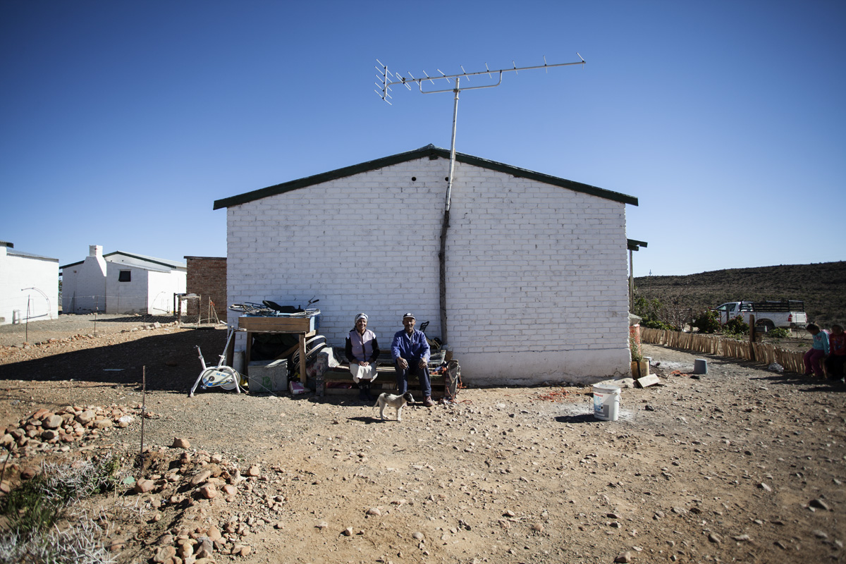Freek Migels en sy vrou Mietjie Migels buite hulle huis op die plaas. Hy is die enigste aandeelhouer wat op die plaas bly. "As 'n mens wil kennis he van 'n plaas en soos ek 'n plaas ken in sy area en sy grond, moet jy op die plaas wees sodat jy kan sien wat gaan daar aan op die plaas."